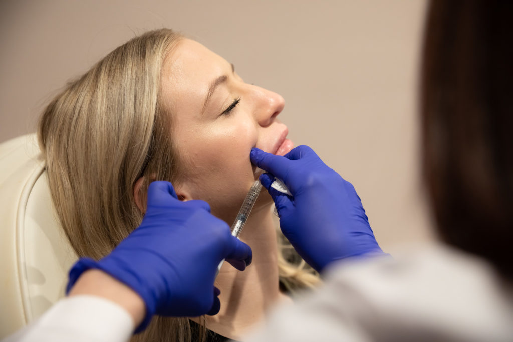 Woman laying back in chair as gloved professional injects lip filler near Winter Garden, FL